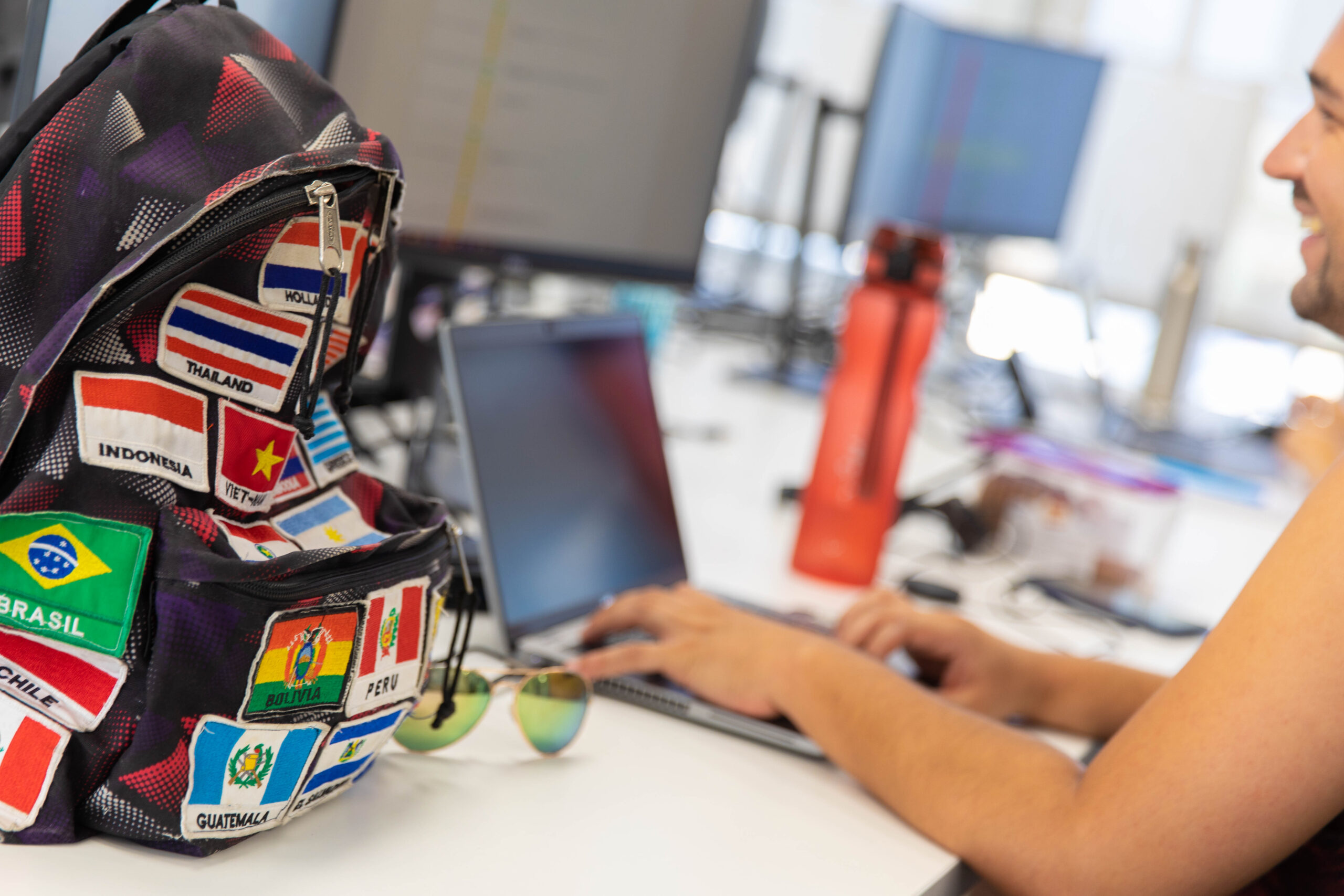 An image of a contact centre worker typing on their laptop. In the foreground you can see a rucksack with flags of the world sewn on.