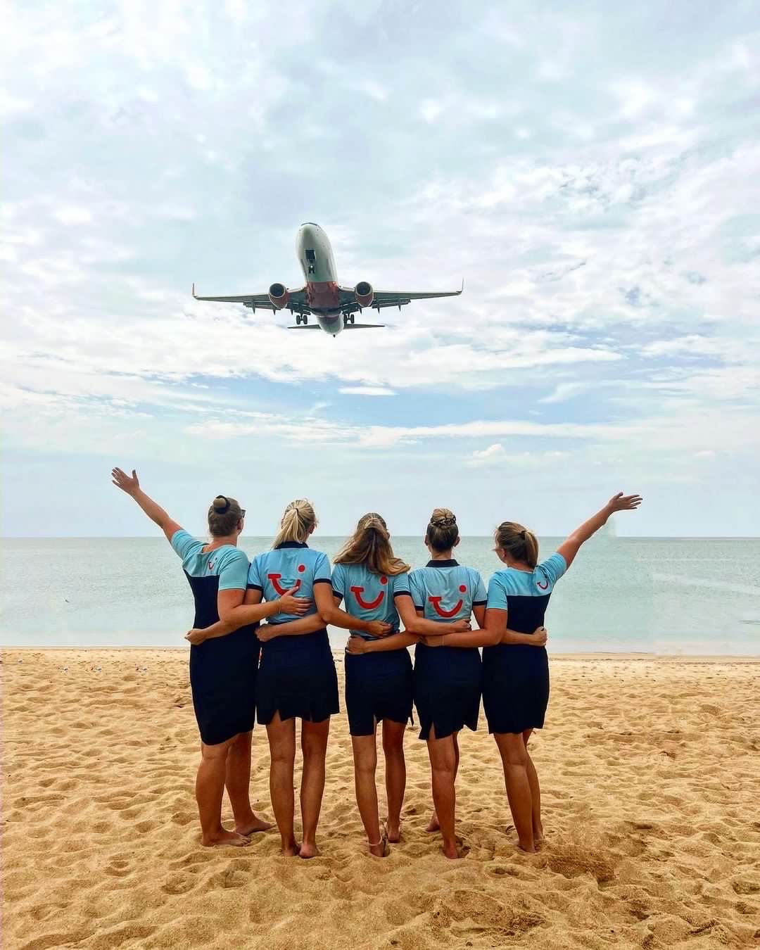 TUI Reps on a beach arm in arm waving at a plane about to go overhead.
