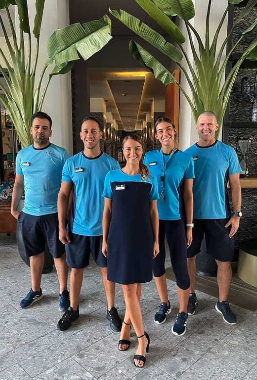 5 Reiseleiter in TUI BLUE Uniform stehen lächelnd vor Palmen
