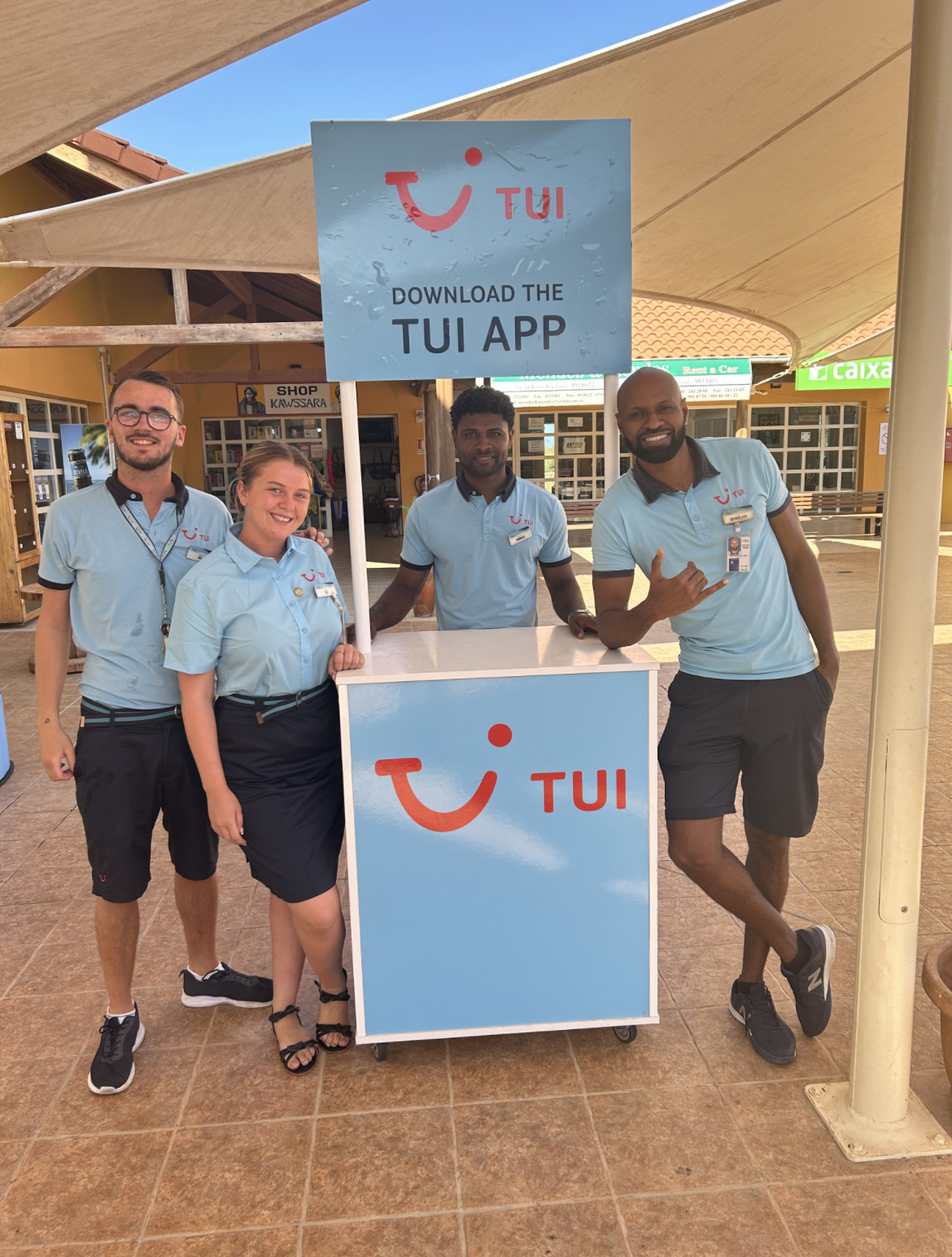 A group of 4 reps standing behind a TUI desk at an airport. They are all wearing uniform smiling at the camera. You can see the airport terminal in the background.