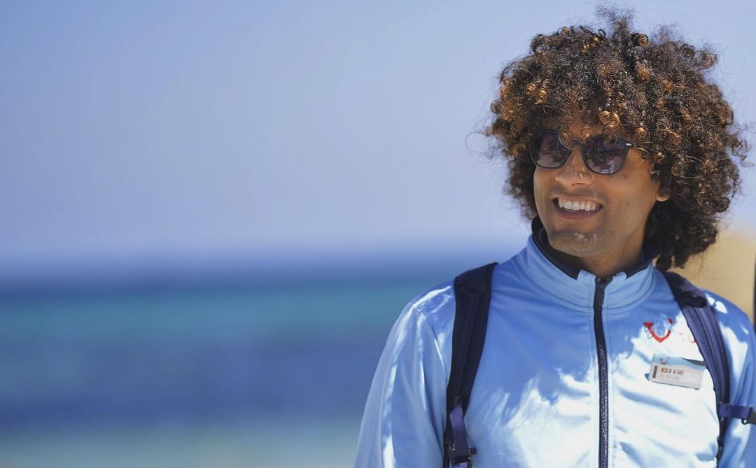 A rep stood on a beach with a blurred sea view behind looking into the distance. The rep has a TUI Uniform on and a Backpack.