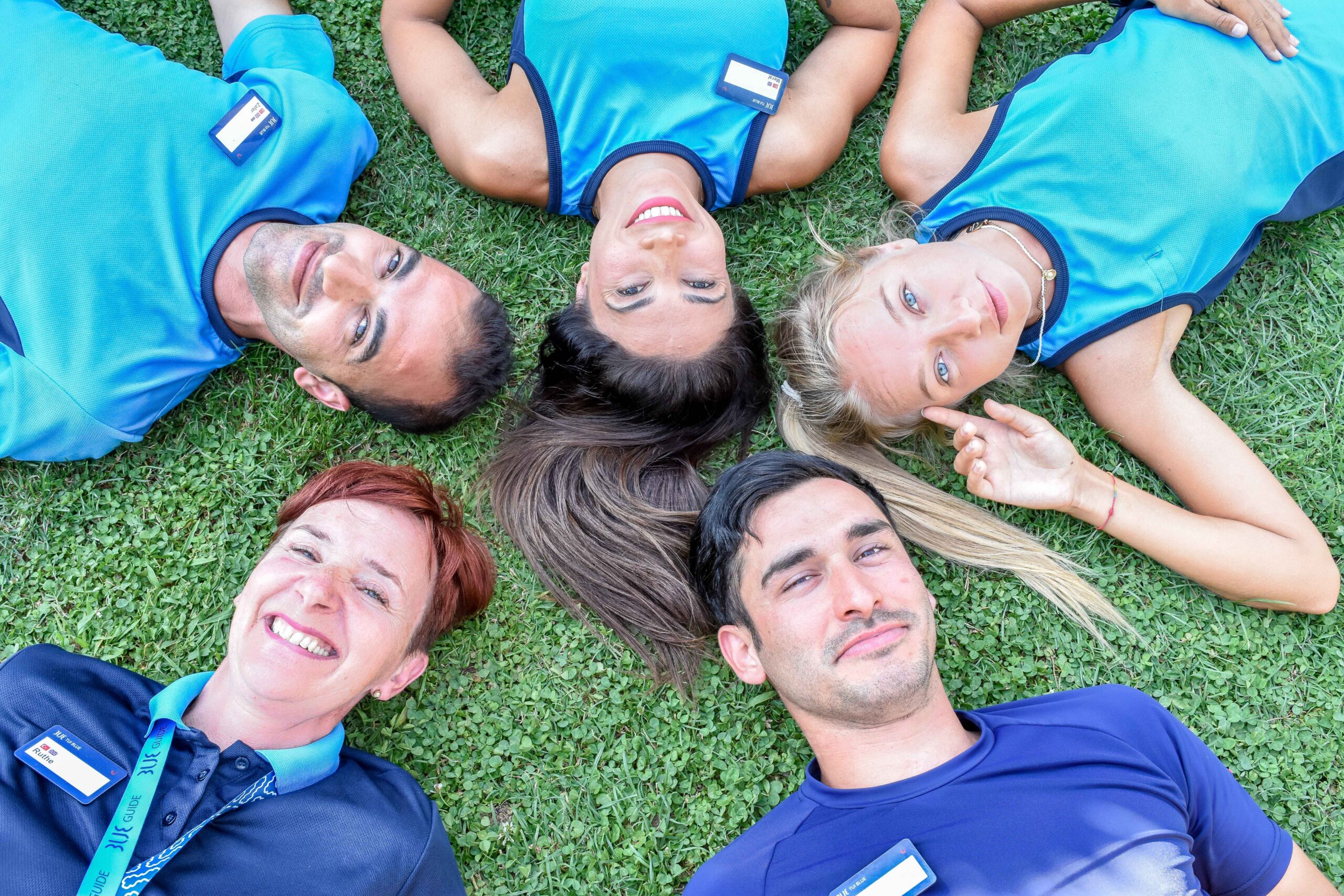 a group of colleagues lay on the floor looking up at the camera. They are smiling with TUI uniforms on.